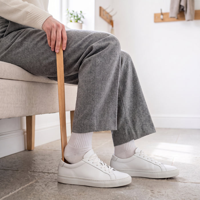 Personne assise qui enfile une basket blanche avec le chausse-pied long, sans se pencher